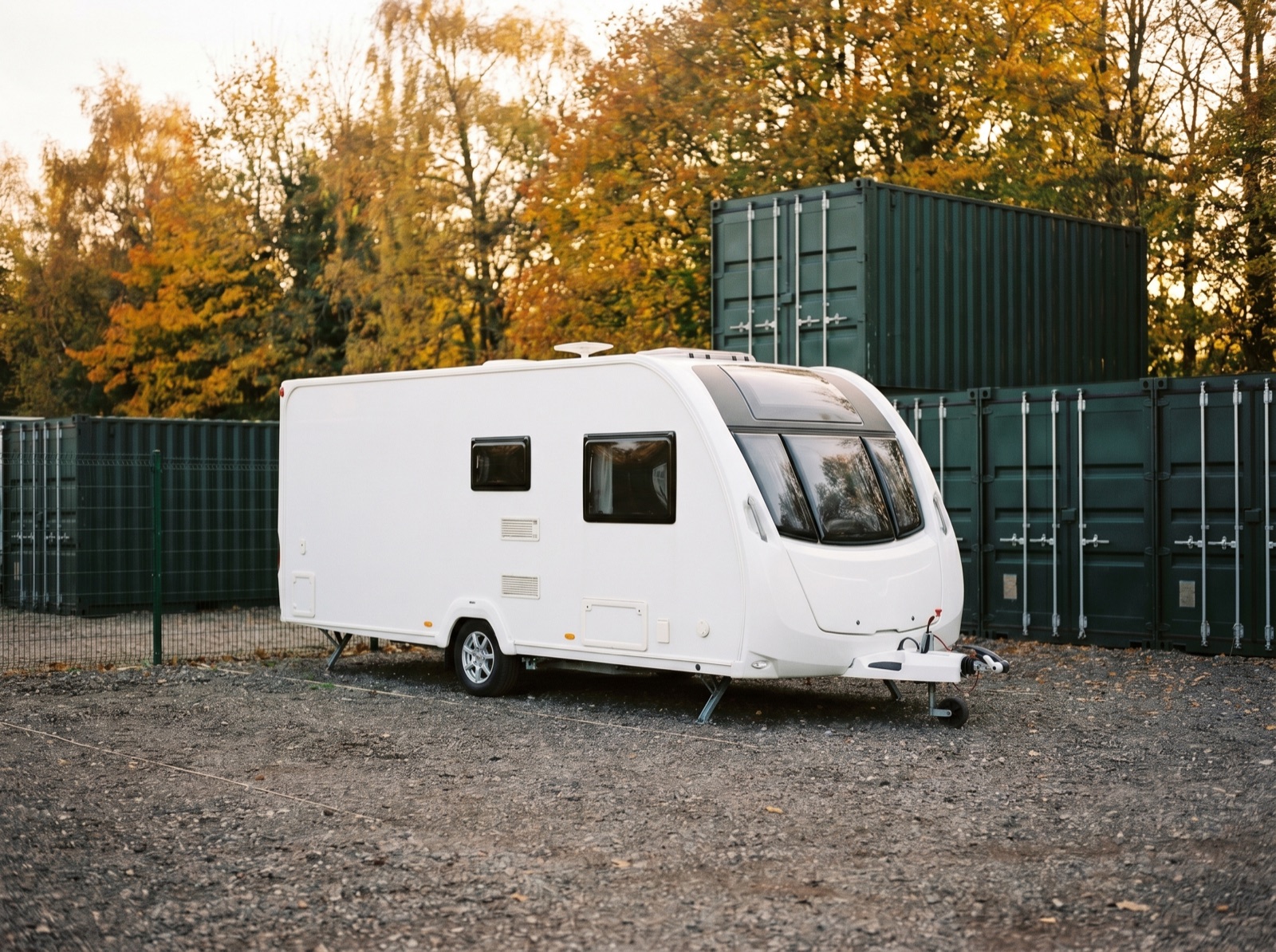 White touring caravan stored at SOS Storage, in front of green shipping containers